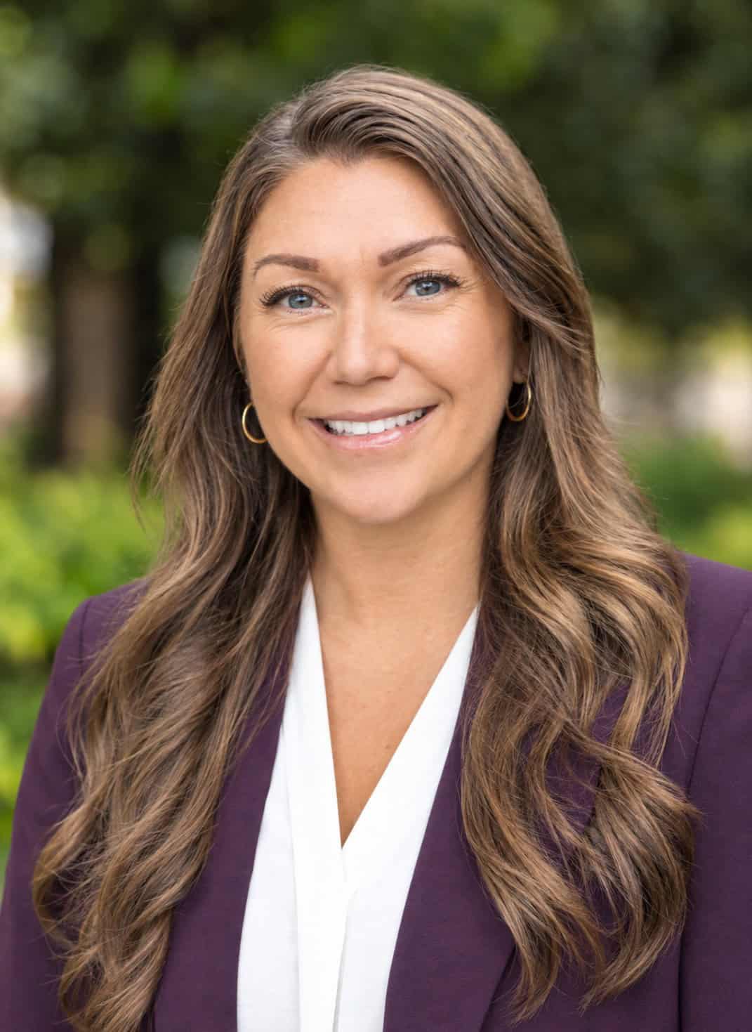 Portrait of Ashley Price smiling outdoors with greenery background.