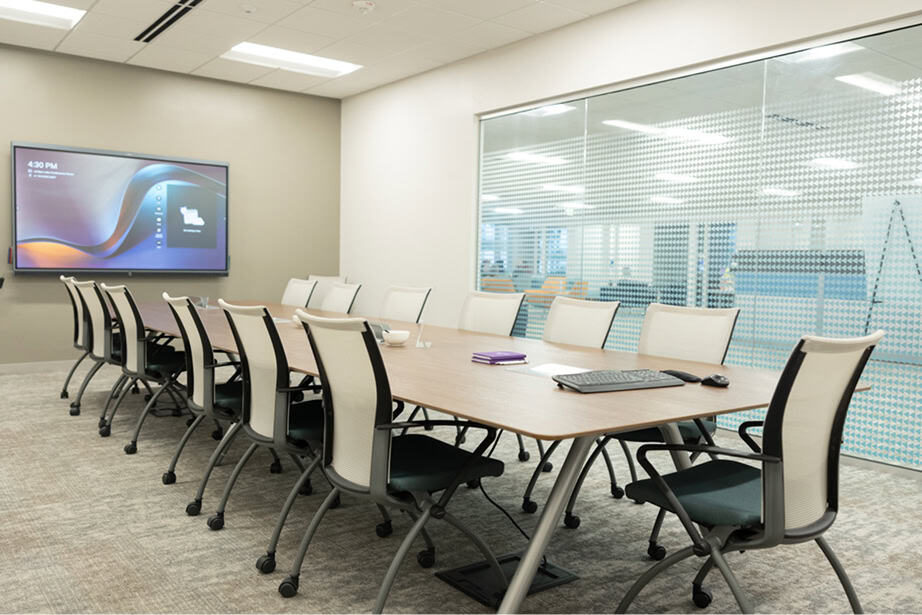 Conference room showing long board table and rolling chairs facing large monitor on the wall.