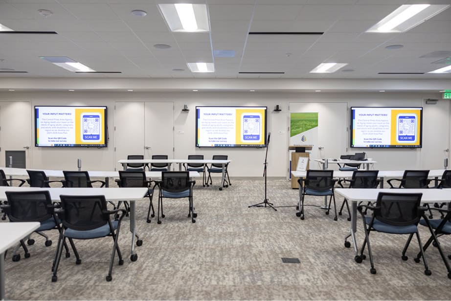 table and chairs shown in empty conference room. TV displays on at front of room.