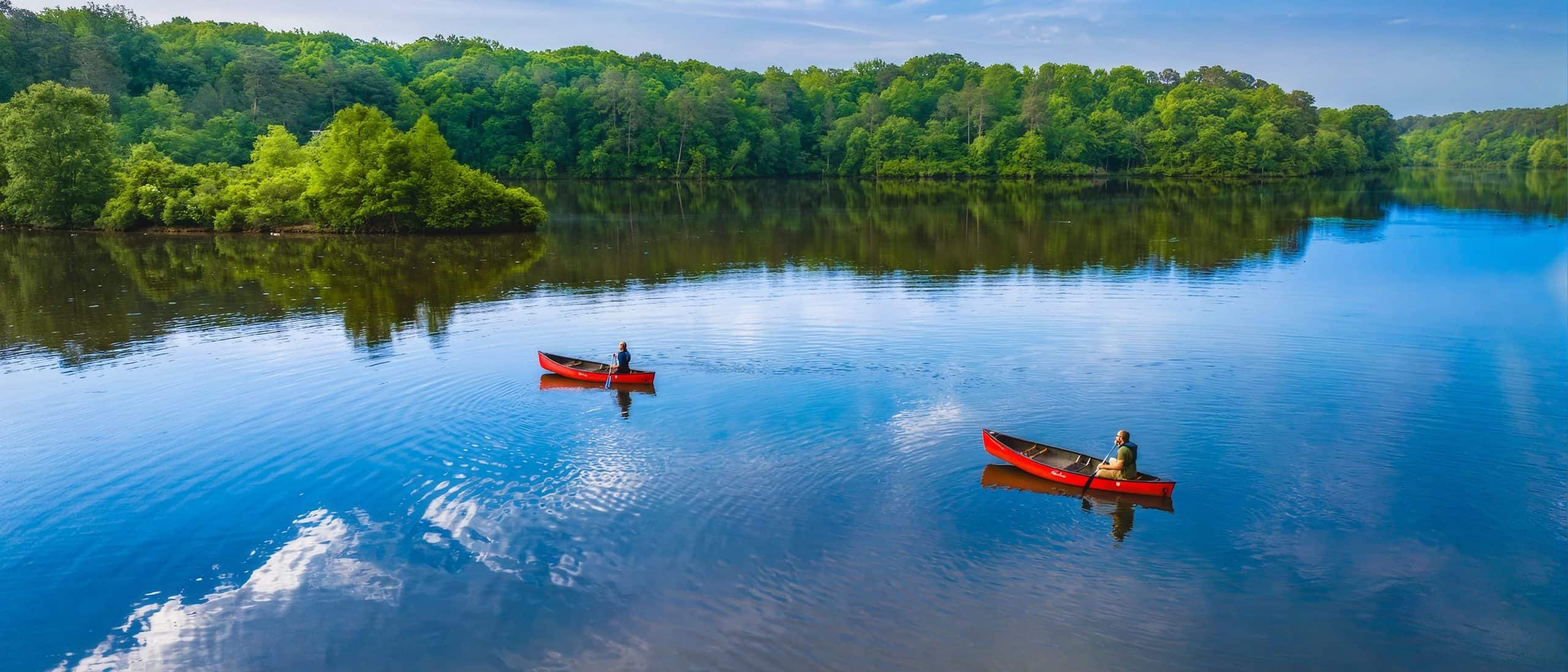 Two individual in canoes. Rowing in a river with trees in the background. 