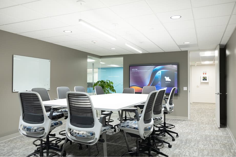 Tall conference room table and chairs facing monitor hanging on wall