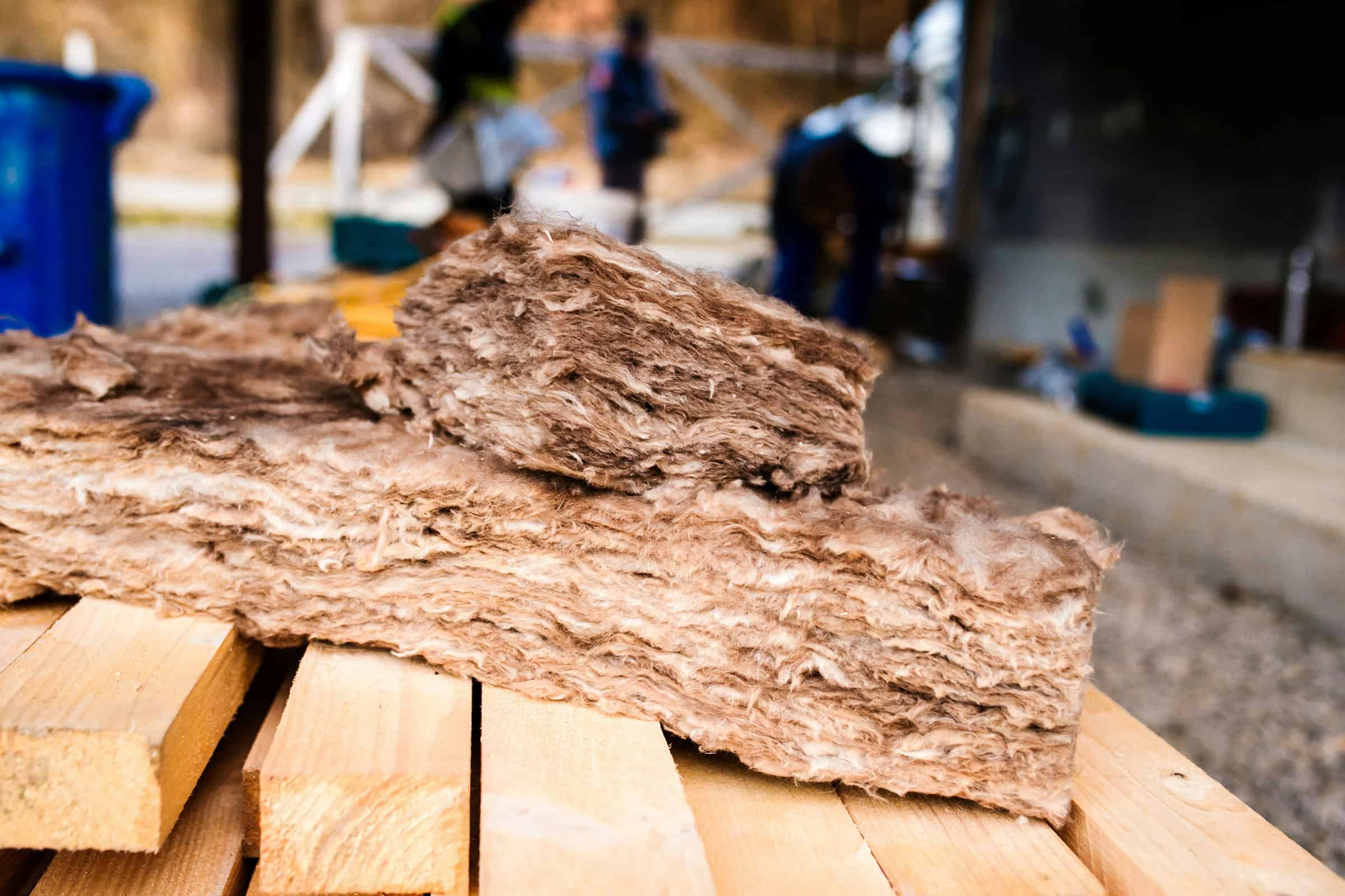Fiberglass insulation batts stacked on lumber at a work site.
