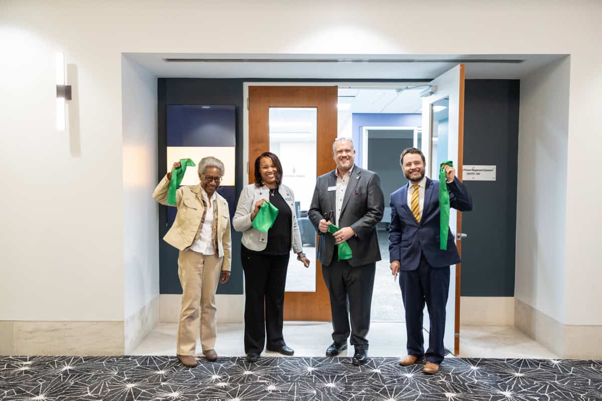 Four people pose in the Central Pines office doorway with pieces of a green ribbon after a ribbon cutting.