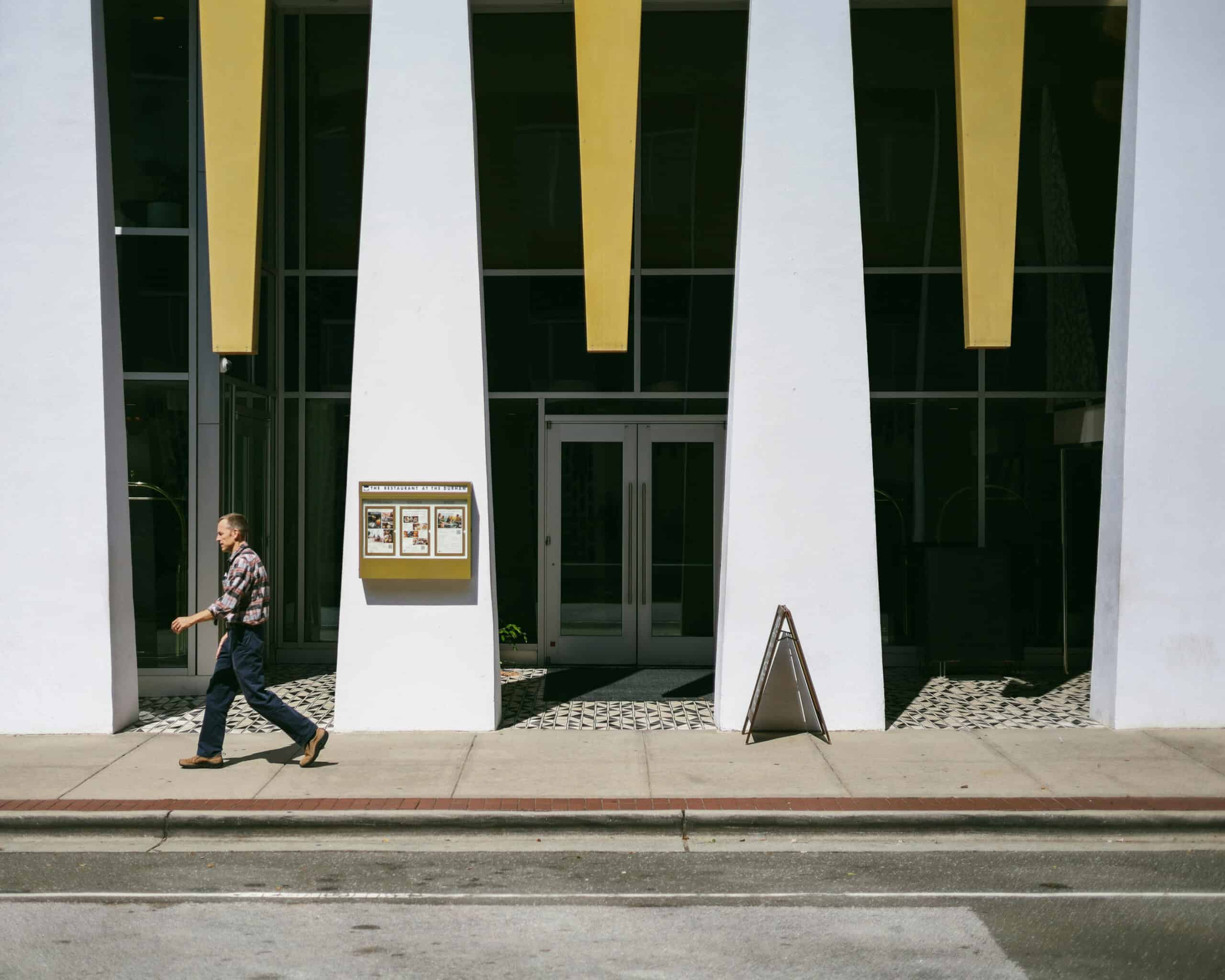 A person walks past tall white columns and gold accents outside The Durham Hotel.