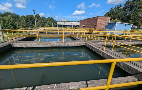 Water treatment basins with yellow safety railings at a facility surrounded by trees.