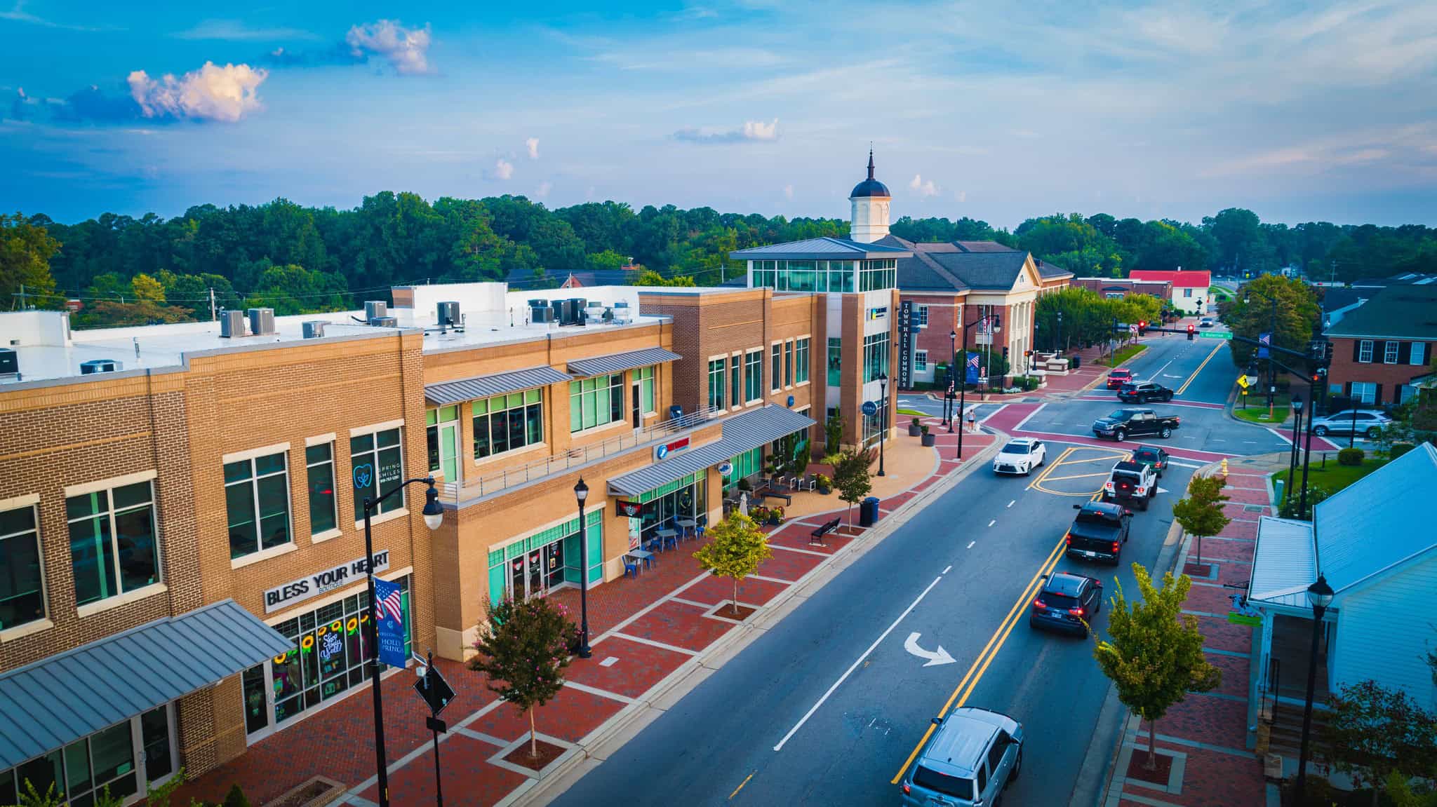 Elevated view of downtown Holly Springs, with brick storefronts, a town building with a cupola and cars traveling along the main street.