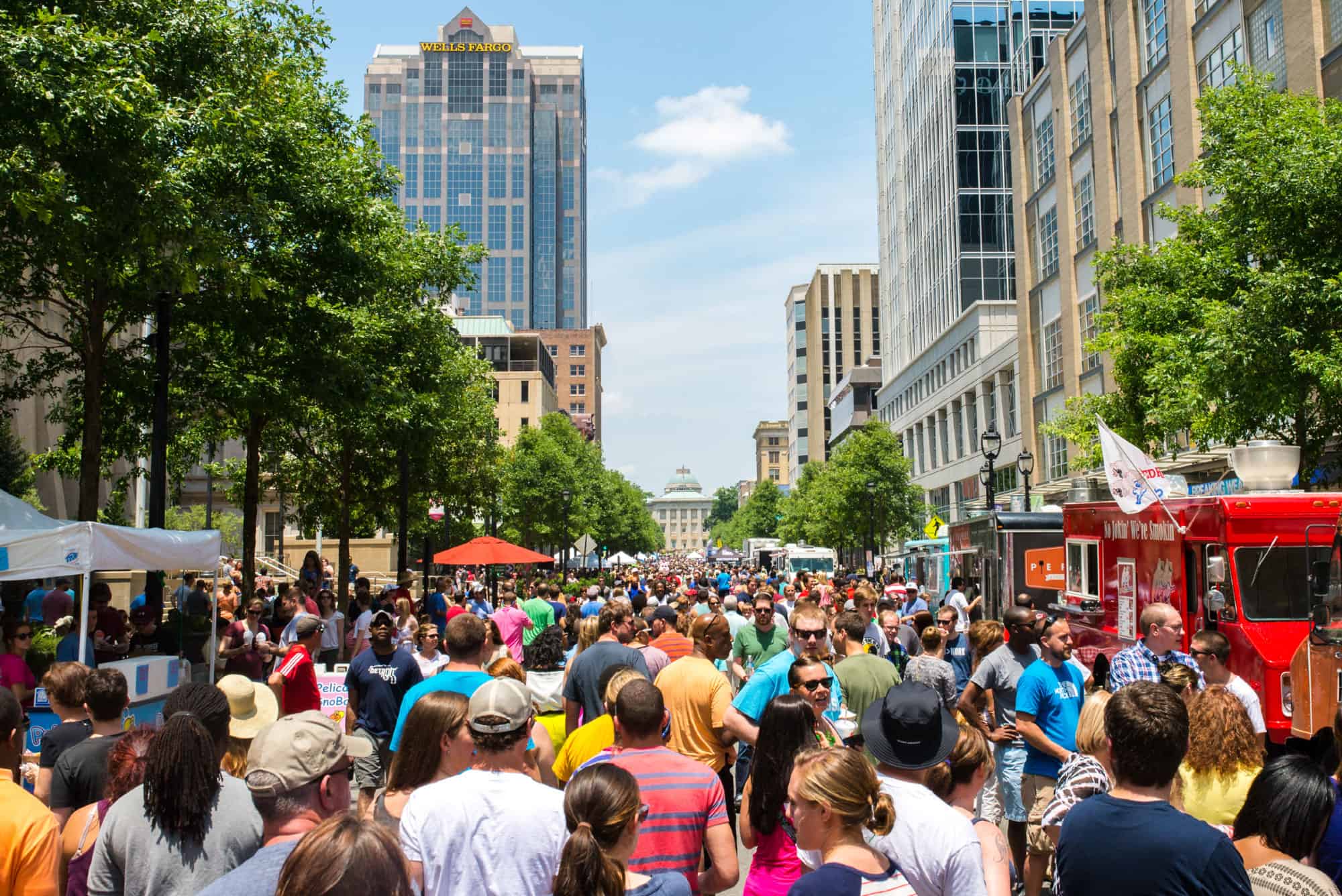 Crowds gather in a street as food trucks line the sides of the road.