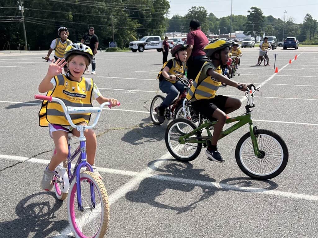 Children ride bicycles in a parking lot.